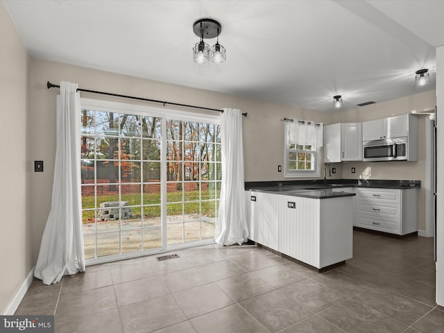 kitchen with white cabinetry, sink, hanging light fixtures, kitchen peninsula, and dark tile patterned flooring