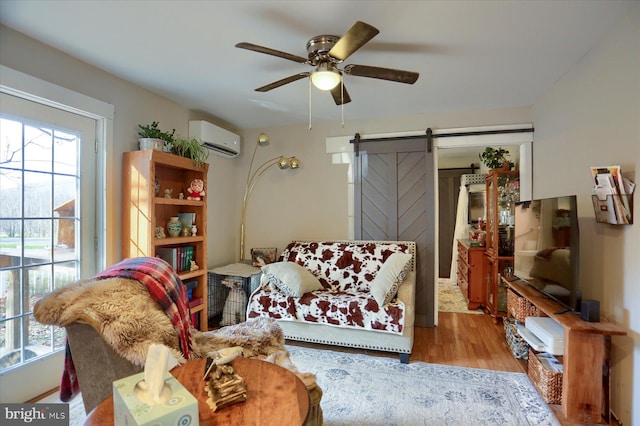 living room with a barn door, light hardwood / wood-style floors, an AC wall unit, and ceiling fan