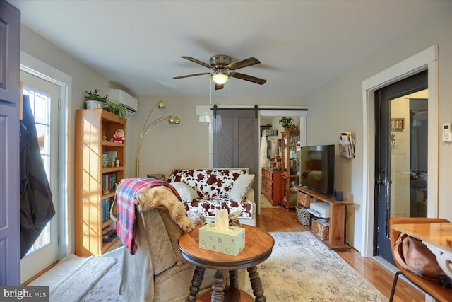 living room featuring ceiling fan, a barn door, a wall mounted AC, and light hardwood / wood-style flooring