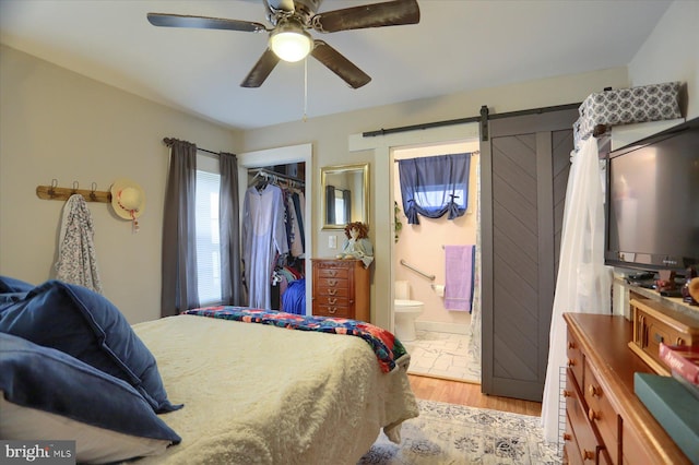 bedroom featuring light hardwood / wood-style flooring, ceiling fan, a barn door, connected bathroom, and a closet