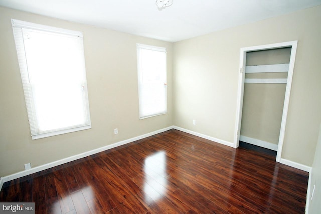 unfurnished bedroom featuring a closet, dark wood-type flooring, and multiple windows