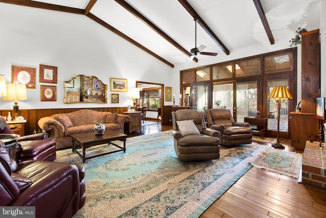 living room featuring ceiling fan, wood-type flooring, beam ceiling, high vaulted ceiling, and wood walls