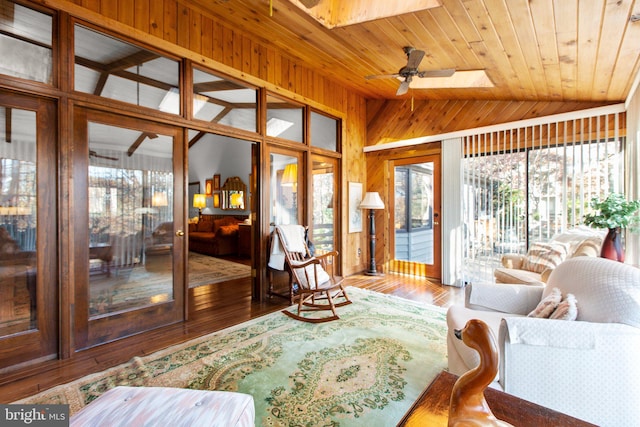 living room featuring ceiling fan, wood-type flooring, wooden walls, vaulted ceiling with skylight, and wood ceiling