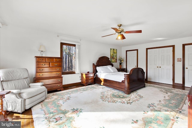 bedroom with two closets, hardwood / wood-style flooring, and ceiling fan