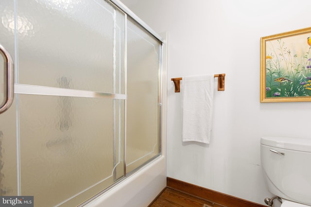 bathroom with wood-type flooring, combined bath / shower with glass door, and toilet