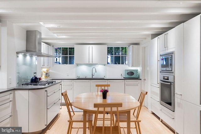 kitchen with light wood-type flooring, white cabinets, appliances with stainless steel finishes, ventilation hood, and sink