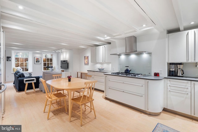 kitchen featuring stainless steel gas stovetop, wall chimney exhaust hood, light hardwood / wood-style flooring, white cabinetry, and tasteful backsplash