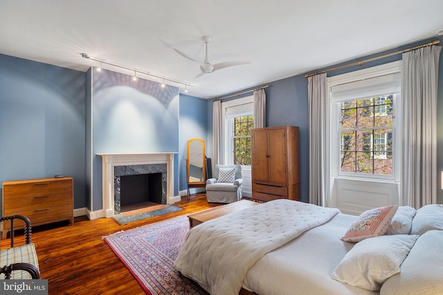 bedroom featuring hardwood / wood-style floors, rail lighting, a premium fireplace, and ceiling fan