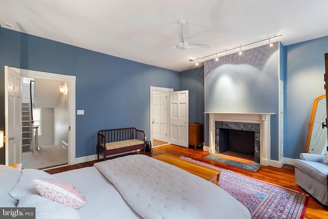 bedroom with track lighting, hardwood / wood-style floors, ceiling fan, and a high end fireplace