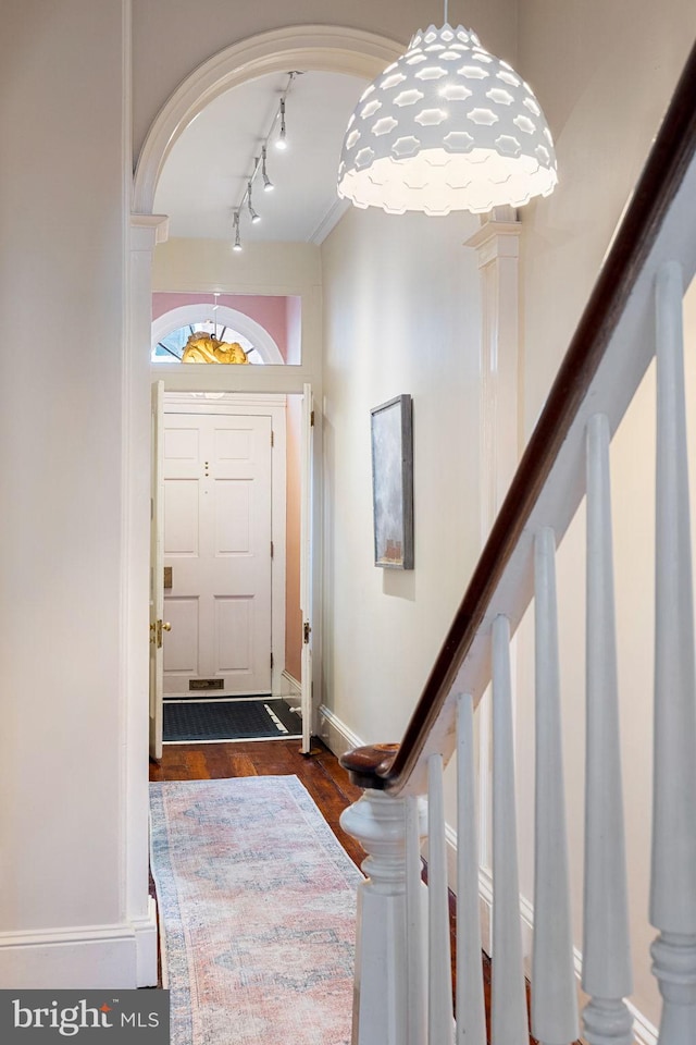 foyer with dark wood-type flooring, track lighting, and crown molding