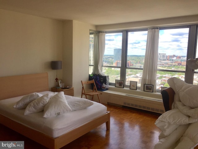 bedroom featuring multiple windows, radiator heating unit, and parquet floors