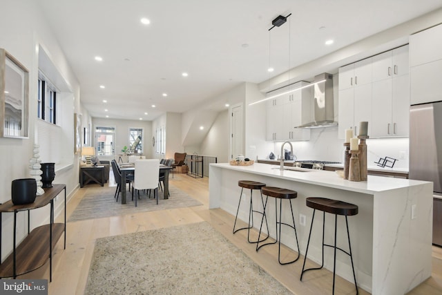 kitchen featuring white cabinets, light hardwood / wood-style flooring, wall chimney exhaust hood, and hanging light fixtures