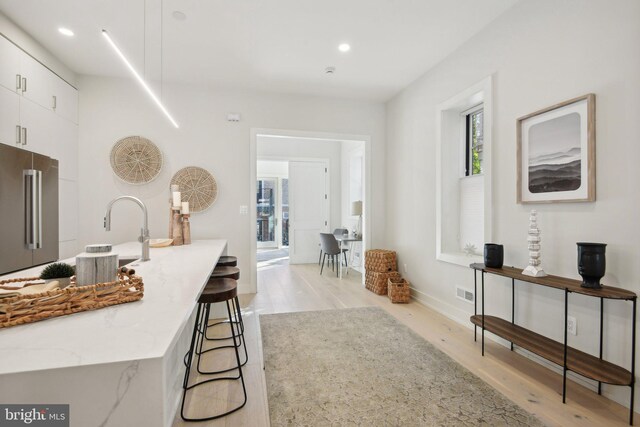 kitchen with light stone countertops, a kitchen breakfast bar, high end refrigerator, white cabinets, and light wood-type flooring