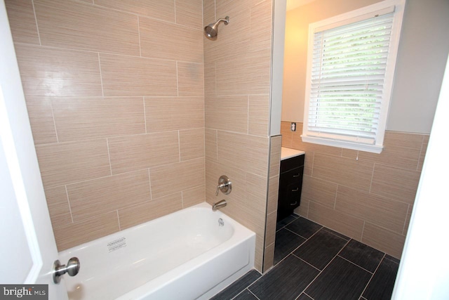 bathroom with tile patterned flooring, vanity, tiled shower / bath combo, and tile walls