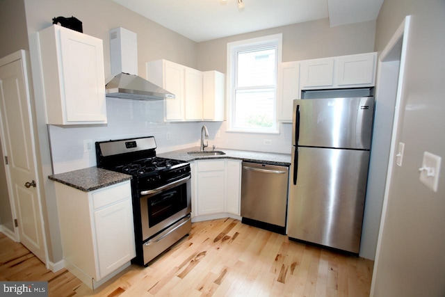 kitchen featuring wall chimney exhaust hood, dark stone countertops, white cabinetry, and appliances with stainless steel finishes