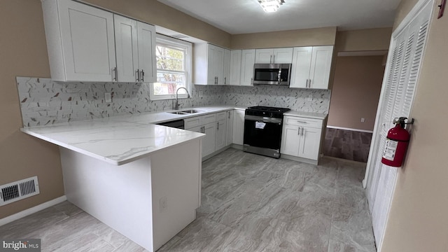 kitchen with kitchen peninsula, sink, light stone countertops, appliances with stainless steel finishes, and white cabinetry