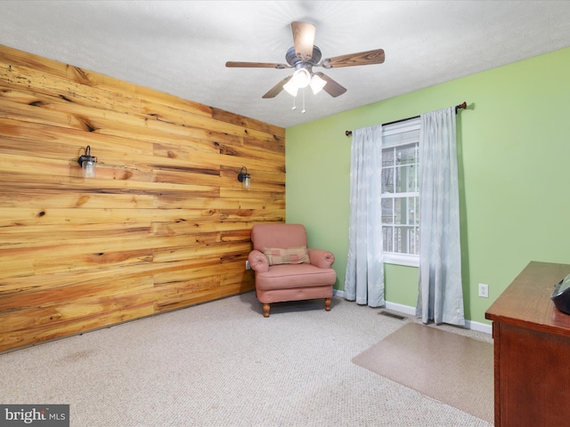 living area with carpet floors, ceiling fan, and wooden walls