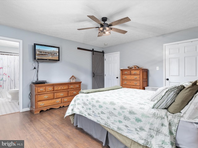 bedroom with ensuite bath, ceiling fan, dark wood-type flooring, a barn door, and a textured ceiling