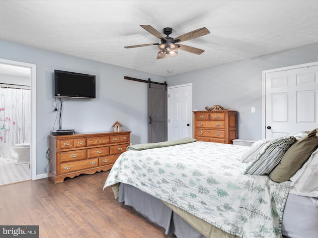 bedroom with ensuite bathroom, dark hardwood / wood-style floors, a barn door, ceiling fan, and a textured ceiling