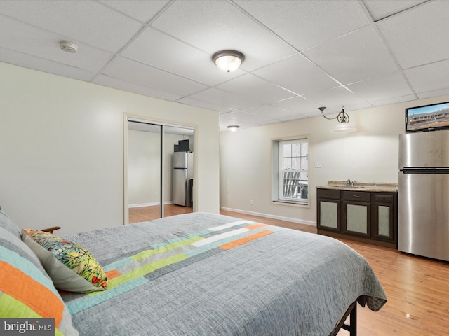 bedroom with light hardwood / wood-style floors, stainless steel refrigerator, a closet, and sink