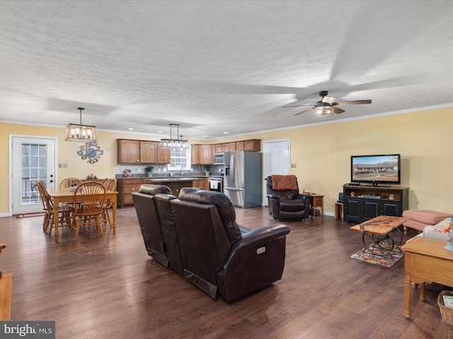 living room featuring a textured ceiling, ceiling fan with notable chandelier, ornamental molding, and dark wood-type flooring