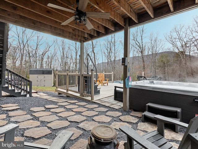 view of patio with ceiling fan, a shed, a deck with mountain view, and a hot tub