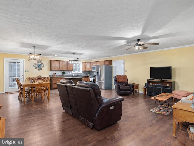 living room with a textured ceiling, dark hardwood / wood-style floors, ornamental molding, and ceiling fan with notable chandelier