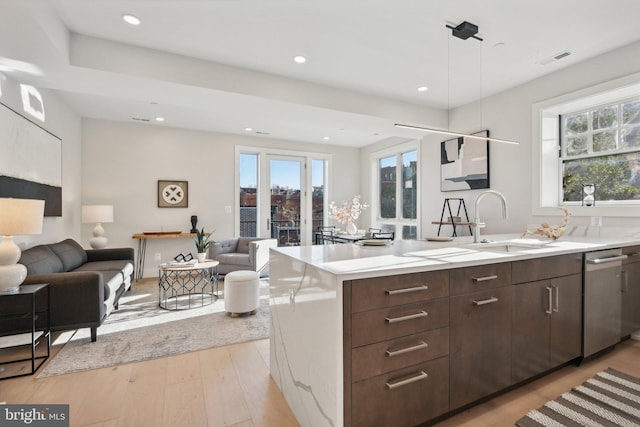 kitchen featuring stainless steel dishwasher, sink, pendant lighting, light hardwood / wood-style floors, and an island with sink