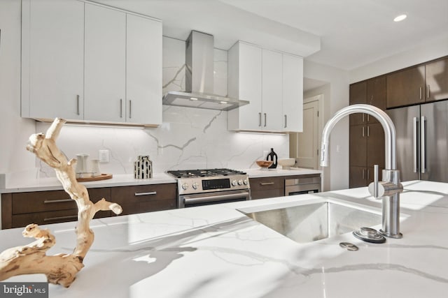 kitchen featuring dark brown cabinetry, light stone countertops, wall chimney exhaust hood, decorative backsplash, and high end appliances