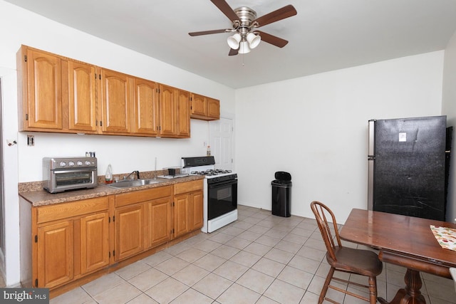 kitchen with light tile patterned floors, range with gas cooktop, ceiling fan, stainless steel refrigerator, and sink