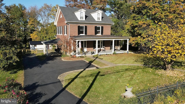 view of front of house with driveway, covered porch, fence, a front lawn, and brick siding