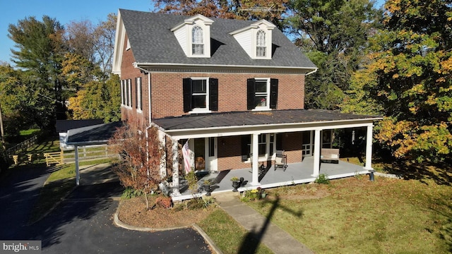 view of front of house featuring covered porch, a shingled roof, a front yard, and brick siding