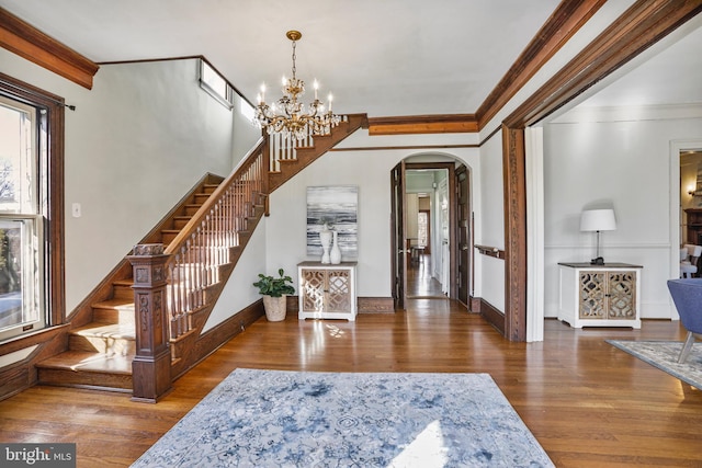 entrance foyer featuring arched walkways, a chandelier, stairway, dark wood finished floors, and crown molding