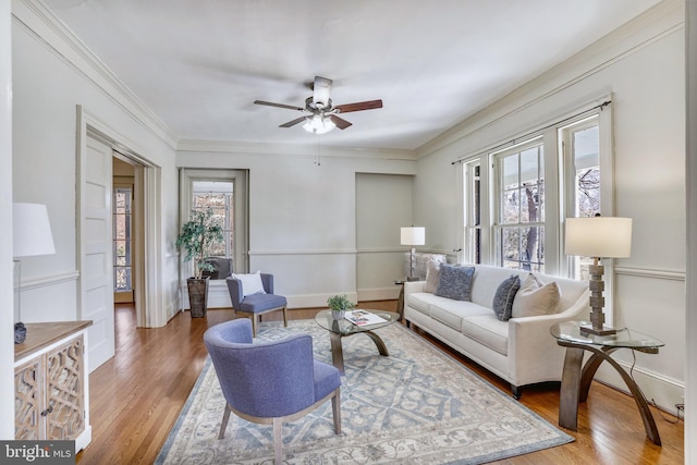 living area featuring light wood-type flooring, ceiling fan, ornamental molding, and baseboards