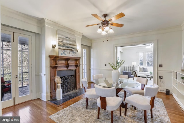 dining space with french doors, a fireplace with raised hearth, crown molding, and wood finished floors