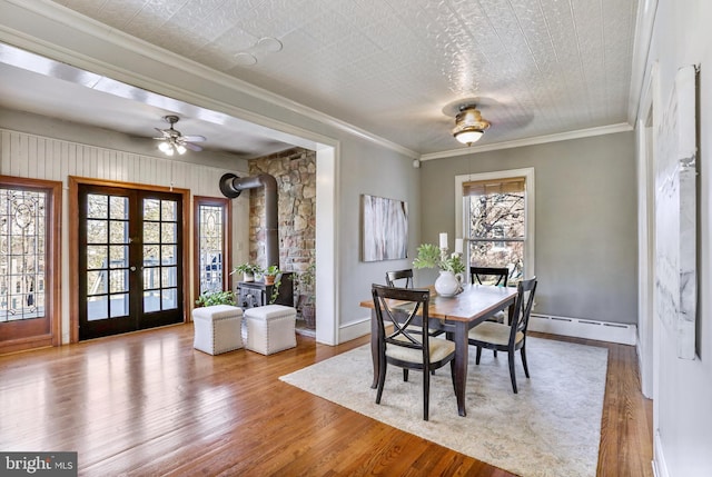 dining area with ornamental molding, light wood-type flooring, french doors, and a baseboard radiator