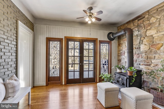 interior space featuring a wood stove, light wood-style flooring, a ceiling fan, and french doors