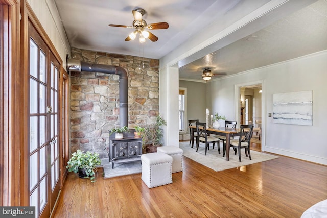 interior space with ornamental molding, a ceiling fan, a wood stove, and light wood-style floors