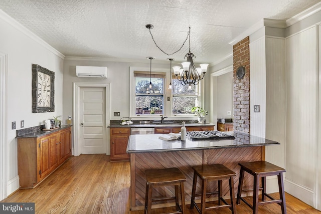 kitchen with brown cabinetry, light wood-style flooring, a breakfast bar area, decorative light fixtures, and a wall mounted AC