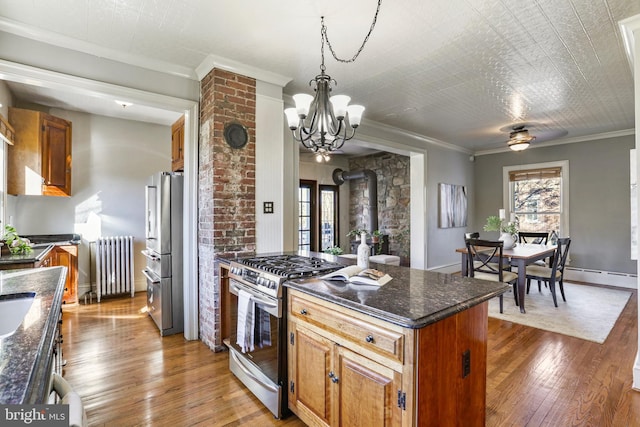 kitchen featuring brown cabinetry, radiator, appliances with stainless steel finishes, a wood stove, and crown molding