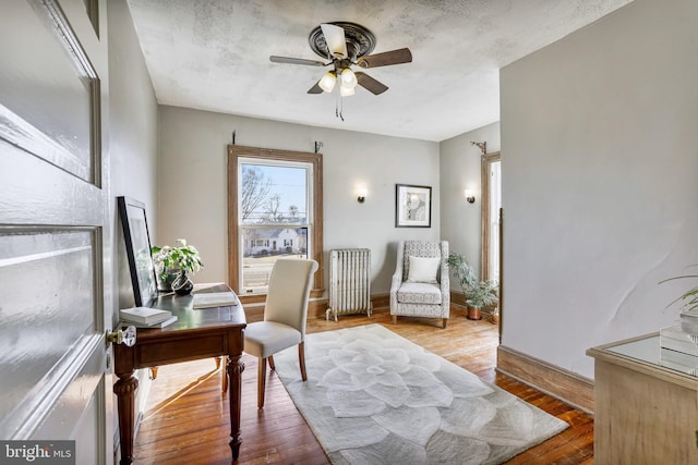 office featuring radiator, ceiling fan, a textured ceiling, light wood-type flooring, and baseboards