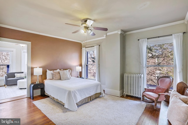 bedroom featuring wood finished floors, a ceiling fan, baseboards, radiator, and crown molding