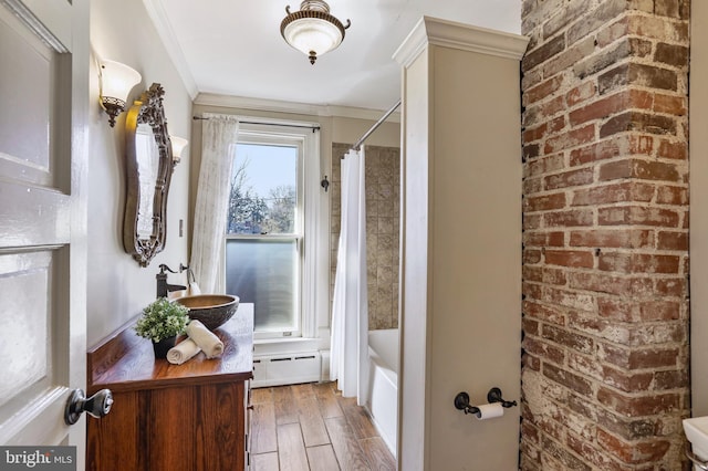 bathroom with crown molding, baseboard heating, shower / bath combo with shower curtain, a sink, and wood finished floors