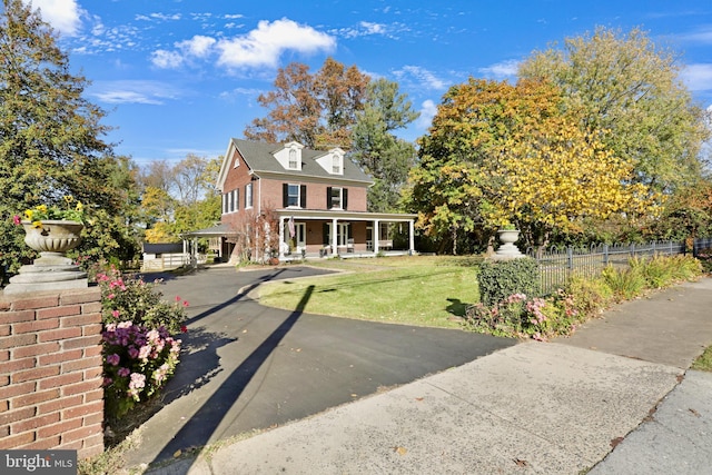 view of front of property with a porch, a front lawn, fence, and brick siding