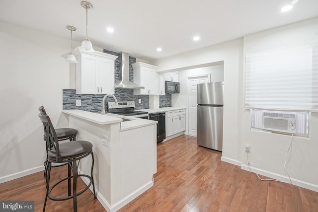 kitchen with kitchen peninsula, wall chimney exhaust hood, white cabinetry, wood-type flooring, and stainless steel appliances