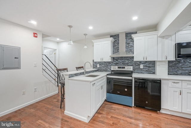 kitchen featuring kitchen peninsula, wall chimney range hood, black appliances, white cabinetry, and hanging light fixtures