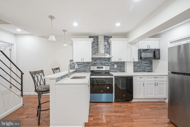 kitchen featuring black appliances, wall chimney range hood, sink, decorative light fixtures, and a kitchen bar