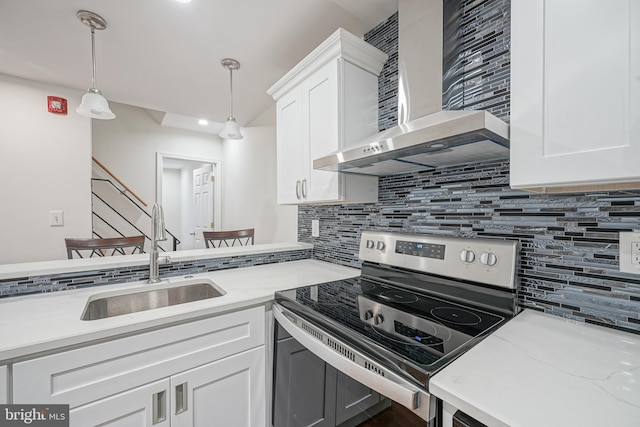 kitchen featuring sink, wall chimney range hood, pendant lighting, white cabinets, and stainless steel electric range oven