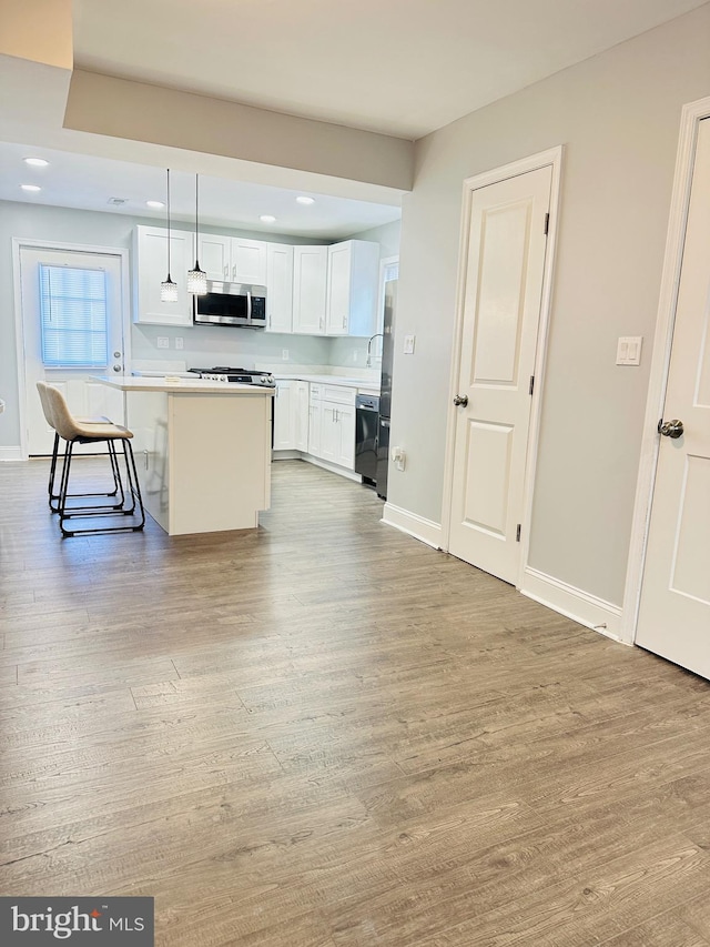 kitchen with a kitchen bar, decorative light fixtures, light hardwood / wood-style flooring, white cabinets, and a center island