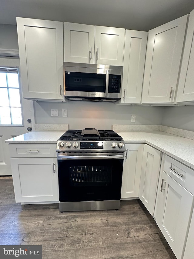 kitchen with white cabinets, stainless steel appliances, light stone counters, and dark wood-type flooring